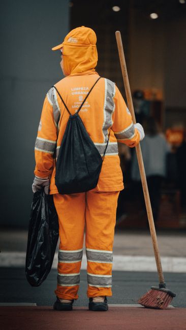 Two professional cleaners from Pimlico Cleaner are performing domestic surface cleaning in a modern living room. One cleaner, on the left, uses a vacuum cleaner on the wooden floor, while the other, o
